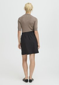 Brun kortærmet sweater parret med en sort stribet nederdel. Nederdelen har en elastisk talje. Modellen bærer flade sorte sko.