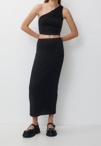 Svart asymmetrisk crop top med rynkad textur, kombinerad med en svart knälång figursydd kjol och kraftiga svarta skor.