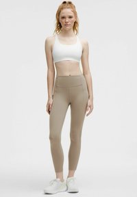 Lättvit sport-bh och beige högmidjade leggings, med slät struktur, åtsittande design, sidofickdetalj och ankellångt snitt.