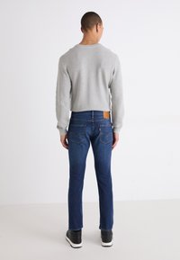 Grå strikket genser, blå denimjeans og svarte joggesko. Ribbestruktur på genseren, lærmerke på jeansene, standard passform.
