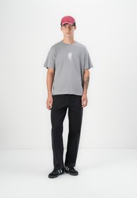 Grå kortærmet t-shirt med en hvid grafik, parret med sorte lige bukser og sorte sportssko med hvide striber. Rød kasket på hovedet.