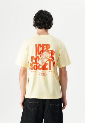 T-shirt en coton jaune avec un design graphique rouge au dos, incluant "ICED COFFEE SOCIETY" et une illustration d'une boisson.