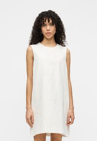 Αμάνικο φόρεμα από ανοιχτό κρεμ ύφασμα με διακριτικό λουλουδάτο μοτίβο. Χαλαρή γραμμή A, στρογγυλή λαιμόκοψη και μήκος μέχρι το γόνατο.