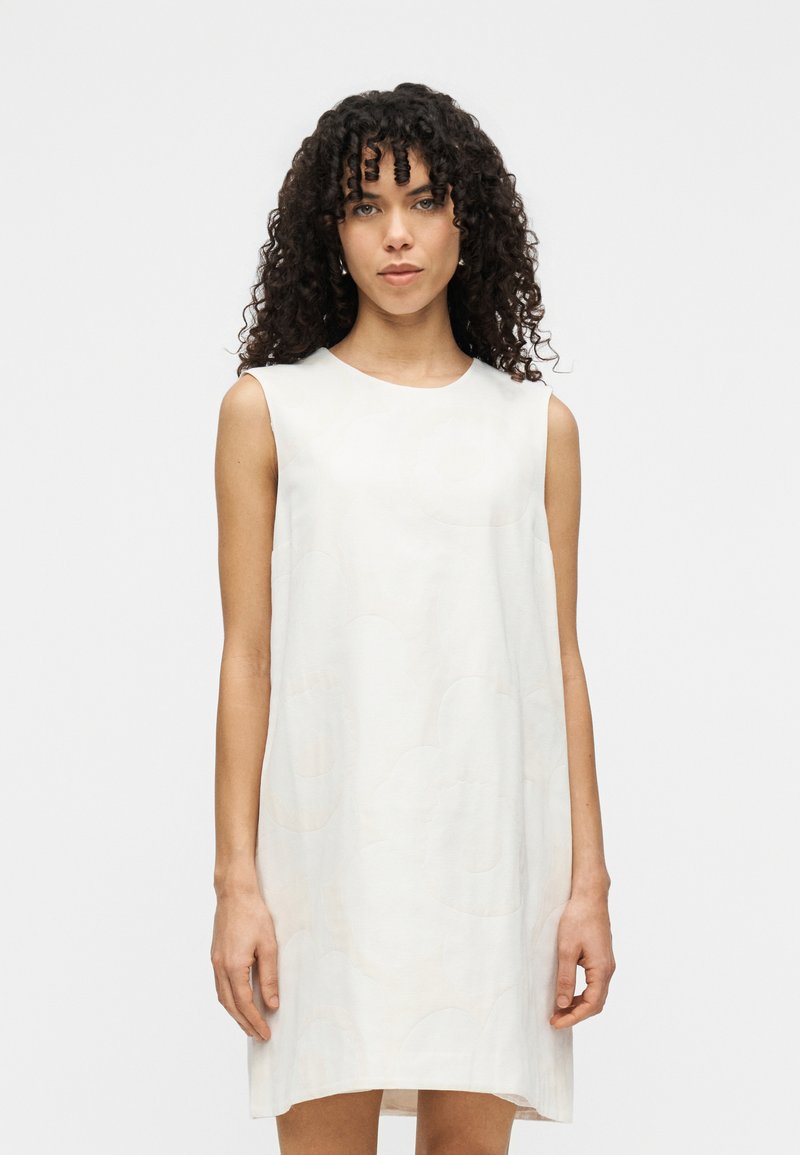 Αμάνικο φόρεμα από ανοιχτό κρεμ ύφασμα με διακριτικό λουλουδάτο μοτίβο. Χαλαρή γραμμή A, στρογγυλή λαιμόκοψη και μήκος μέχρι το γόνατο.