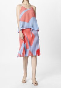 Plisséjurk met een gelaagd ontwerp in rood en blauw. De stof heeft een gladde textuur, met dunne bandjes en een vloeiende silhouet.