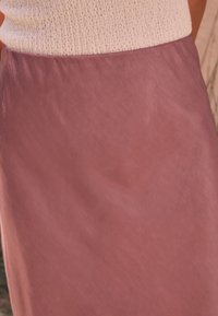 Let nederdel lavet af blødt, flydende stof i en afdæmpet rosafarve med en subtil glans og minimalistisk design.