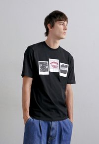 T-shirt en coton noir avec trois impressions graphiques : épingle de sécurité, lèvres et texte "Moschino". Col rond, manches courtes, coupe décontractée.