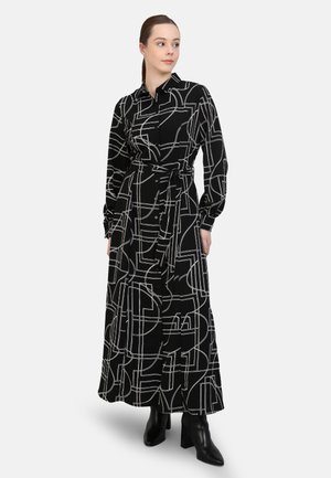 Black long-sleeve dress with white geometric patterns, button-down front, waist belt, and a flowing silhouette. Worn with black ankle boots.