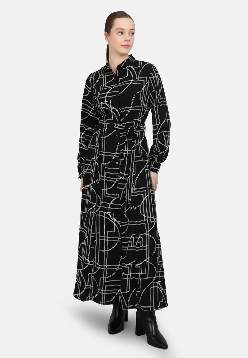 Black long-sleeve dress with white geometric patterns, button-down front, waist belt, and a flowing silhouette. Worn with black ankle boots.