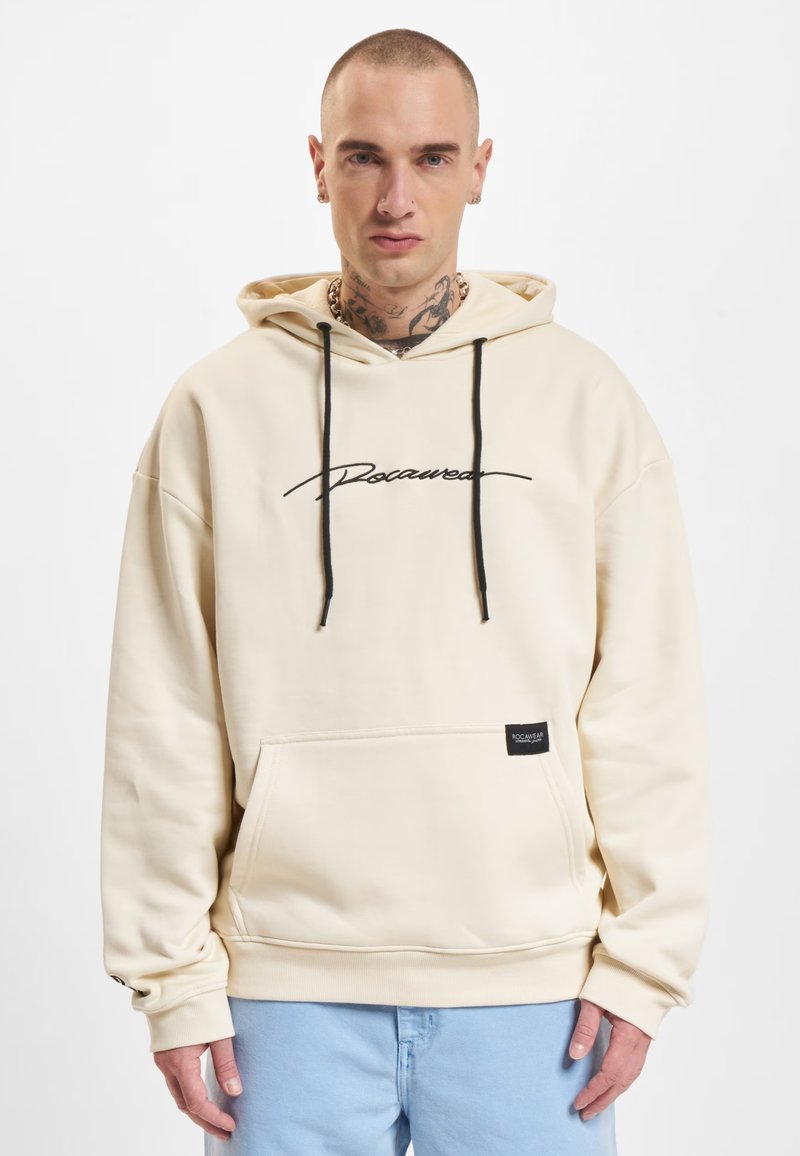 Felpa beige con cappuccio e coulisse, dotata di un logo ricamato nero e una tasca frontale. Tessuto morbido con polsini a costine.