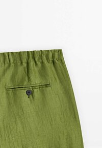 Green fabric pants with elastic waistband and single back pocket with a black button, shown against a white background.
