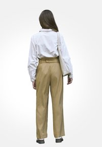 Pasiasta koszula z długim rękawem w kolorze białym i jasnoniebieskim, zestawiona z_brzoskwiniowymi spodniami o wysokim stanie. Ubranie uzupełnia jasna torba na ramię.