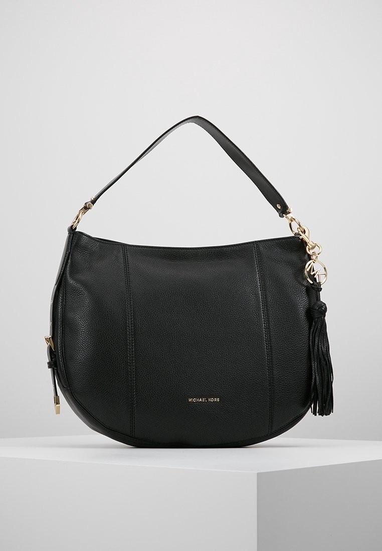 Sac bandoulière en cuir noir avec ferrures dorées, détail pompon et poignée courte, présenté sur un socle blanc sur fond neutre.