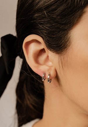 Silberne Creolen, klein und rund, mit glänzender Oberfläche. Worn in der unteren Ohrläppchen, zeigen eine glatte Fläche und ein einfaches Design.