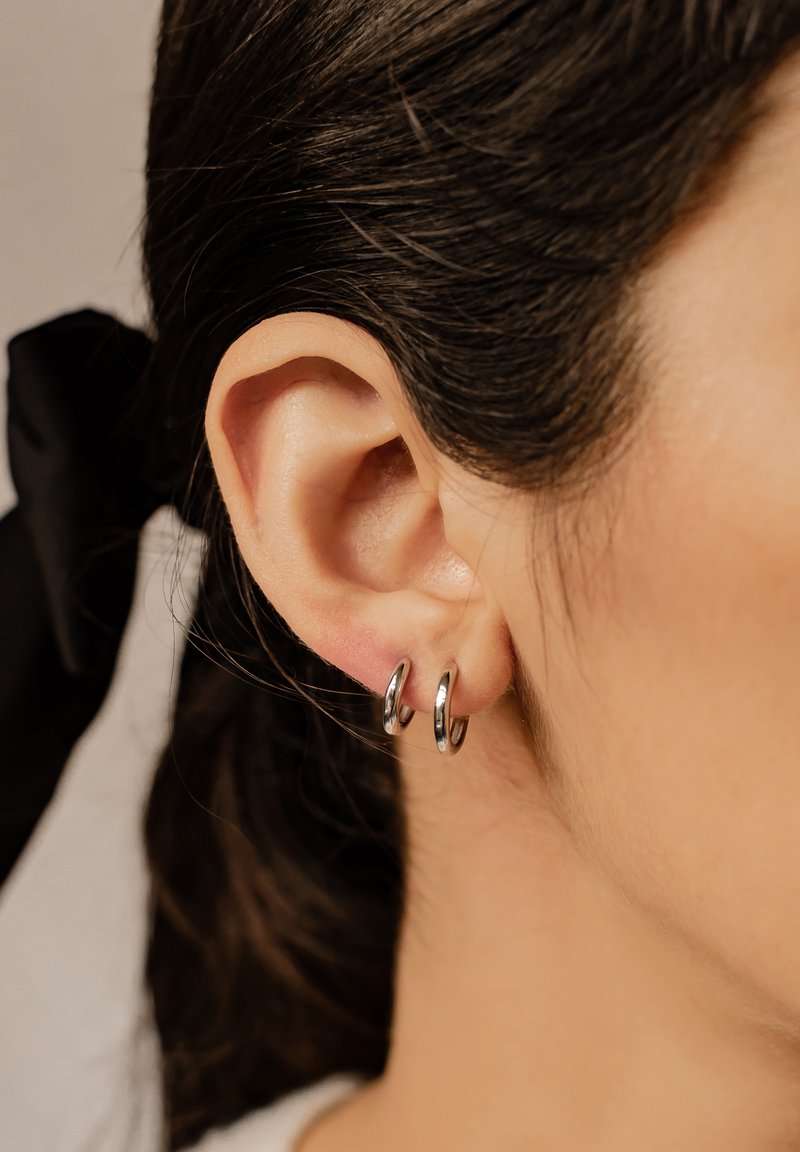 Srebrne kolczyki w formie małych, okrągłych obręczy, o błyszczącej powierzchni. Noszone w dolnej części płatka ucha, prezentujące gładką powierzchnię i prosty design.