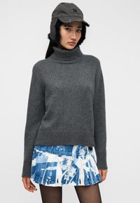 Γκρι πλεκτό πουλόβερ ζιβάγκο με ριμπ τελείωμα, συνδυασμένο με μπλε και λευκή πλισέ μίνι φούστα με αφηρημένα σχέδια. Καπέλο με αυτιά καλυμμένα.