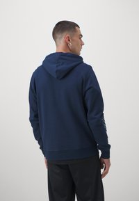 Sweat-shirt à capuche bleu marine en mélange de coton doux ; doté d'une poche kangourou et de poignets élastiques, avec un logo imprimé sur la manche gauche.