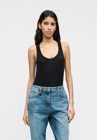 Μαύρο αμάνικο κορμάκι με στρογγυλή λαιμόκοψη και διακριτικό λογότυπο, συνδυασμένο με ανοιχτό μπλε τζιν ψηλόμεσο παντελόνι με εμπρόσθιες τσέπες.