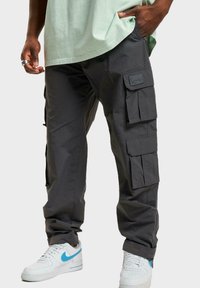 Cargo pants in dark gray fabric with multiple side pockets, a smooth texture, and a relaxed fit, paired with white sneakers featuring blue accents.