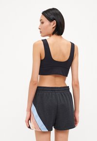 Sostén deportivo negro con espalda de corte redondo, combinado con shorts oscuros de color gris que presentan un patrón diagonal en tonos pastel. El material parece suave con cintura elástica.