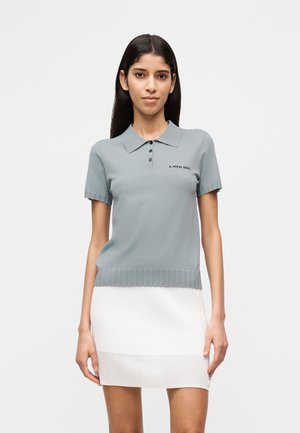 Polo gris clair en matière tricotée douce, doté d'un ourlet côtelé, de manches courtes, d'une patte à trois boutons et d'un logo brodé.