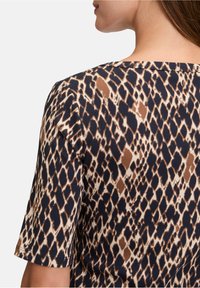 T-shirt à manches courtes avec un imprimé animal texturé dans des tons de marron, beige et marine, avec un large col et un tissu côtelé.