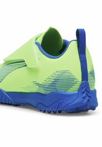 Green athletic shoe with blue accents, textured material, hook-and-loop closure, and a distinct stripe pattern along the side.