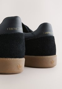 Črni usnjeni in semiš supergi z gumijastim podplatom, z zlatim reliefnim napisom in majhno krono na peti.