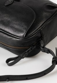 Borsa a tracolla in pelle nera con superficie testurizzata, chiusura con zip e dettagli in bronzo sulla cerniera; presenta una tracolla removibile.