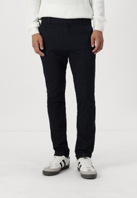 Mörkblå skräddarsydda byxor tillverkade av texturerat tyg, med knäppning och smal passform, parat med grå och vita sneakers.