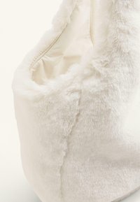 Bijela torbica od umjetnog krzna s mekanom teksturom, zaobljenim oblikom i glatkom unutarnjom podlogom. Ima jednostavan dizajn bez detalja s hardverom.