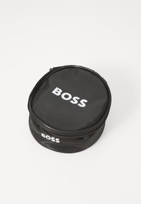 Sac rond noir en tissu texturé avec fermeture éclair. Présente le logo blanc "BOSS" imprimé sur le dessus et sur le côté.