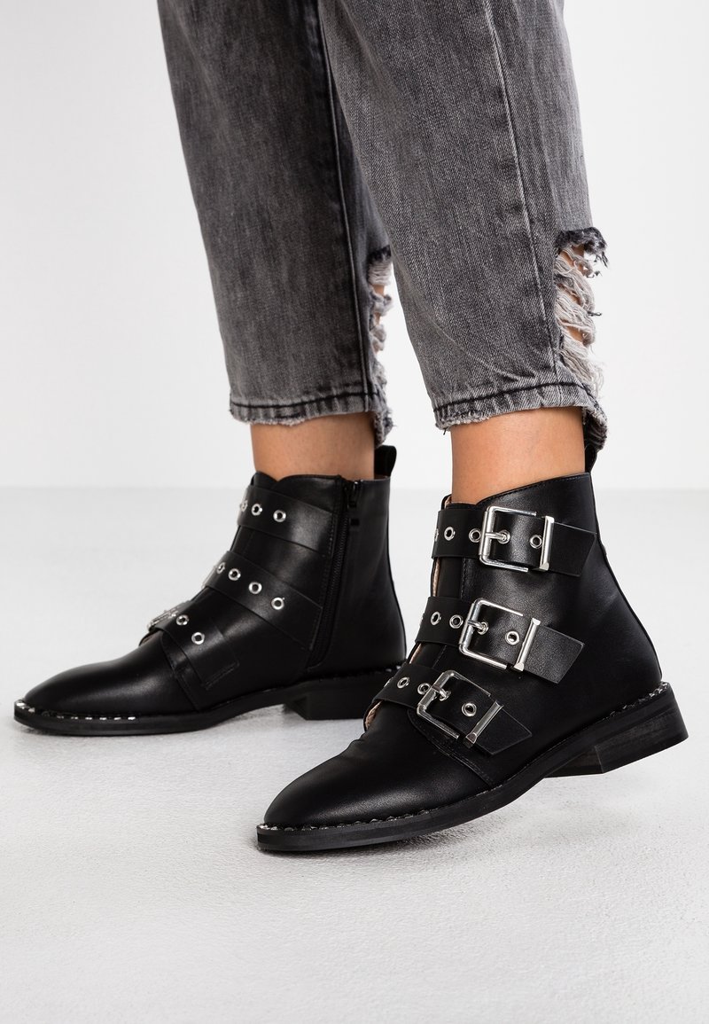 Bottes basses en cuir noir avec trois boucles argentées portées avec un jean gris effiloché.