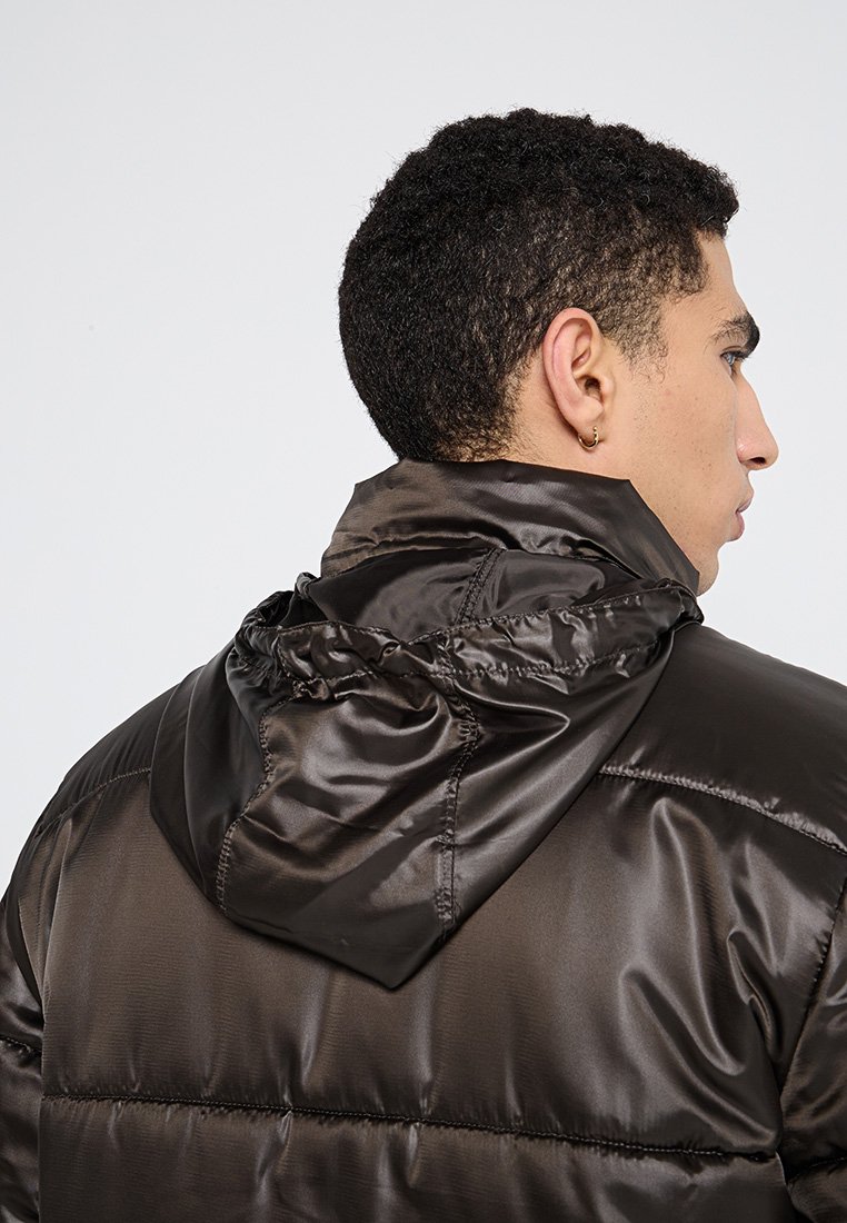 Giacca imbottita marrone con una texture lucida e liscia. Presenta un cappuccio e un motivo a cucitura orizzontale, vista da un angolo laterale.