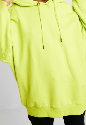 Felpa verde neon realizzata in morbido tessuto, con un ampio cappuccio, lacci regolabili con punte in metallo e una vestibilità comoda.