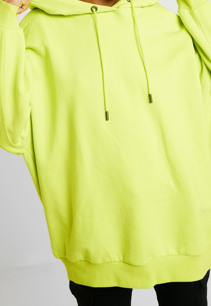 Felpa verde neon realizzata in morbido tessuto, con un ampio cappuccio, lacci regolabili con punte in metallo e una vestibilità comoda.