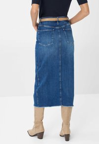 Denim midi rok met een rafelzoom, voorzien van twee achterzakken en een hoge tailleband. Gepaard met knie-hoge beige laarzen.