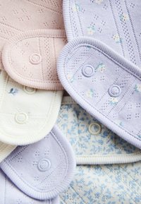 Mäkké pastelové pletené bavlnené deky s patentkami v rôznych svetlých farbách a jemnými kvetinovými vzormi, prekrývajúce sa navzájom.