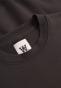 Tamno sivi dukserica s okruglim izrezom, sa ovratnikom i bijelim oznakom branda s crnim dvostrukim W logom unutar izreza.