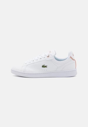 Hvid lavtop sneakers med hvide snørebånd, grønt krokodillelogo på siden og lyserød detalje på hæl og øjer på hvid baggrund.
