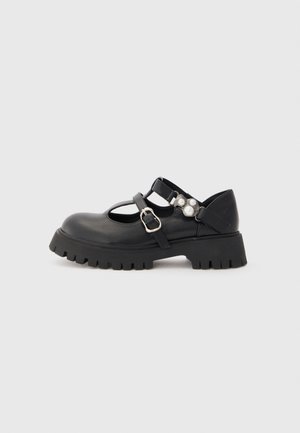 Black leather Mary Jane shoes with a rounded toe, adjustable straps, chunky rubber sole, and pearl accents on the side.