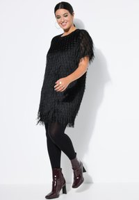 Abito nero con frange, maniche corte e scollatura rotonda, abbinato a leggings neri e stivaletti alla caviglia lucidi color bordeaux.