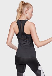 Top atlético negro sin mangas con un panel de malla en la espalda, diseño ajustado y tirantes delgados. Combinado con leggings negros con patrones geométricos.