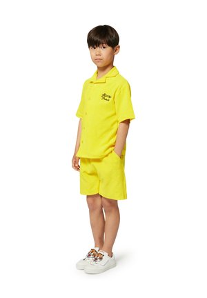 Une chemise jaune en éponge à manches courtes avec des boutons et une broderie "Glen Paris", associée à un short assorti et des baskets blanches avec des accents graphiques.