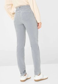 Pantaloni in corduroy grigi con vestibilità slim, dotati di tasche posteriori e una texture liscia, abbinati a sneakers bianche con accenti metallici.