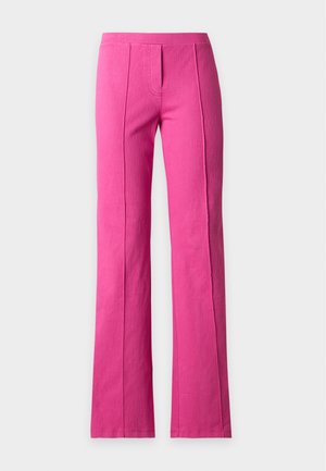 Vrouw draagt felroze broek en een losse, meerkleurige gestreepte top met driekwart mouwen, staat in neutrale sandalen met hoge hakken.