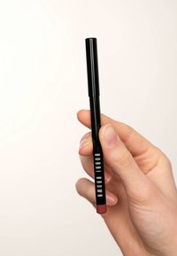 Crayon à lèvres Bobbi Brown dans un tube noir mince et à rotation, avec une teinte rouge-brun riche au bout et une marque claire sur le côté.