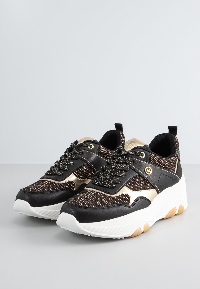 Sneaker nere e dorate con tomaia in maglia testurizzata, dettagli metallici e suola bianca spessa con un pattern di grip in gomma.