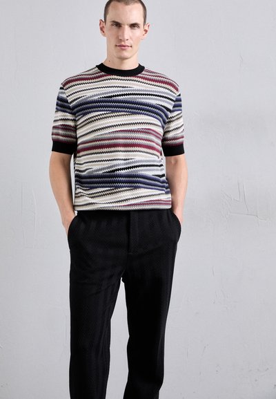 Adīts īsās piedurknes džemperis ar daudzkrāsu zigzaga rakstu, melnu apdari, kombinēts ar melnām teksturētām biksēm ar herringbone rakstu.