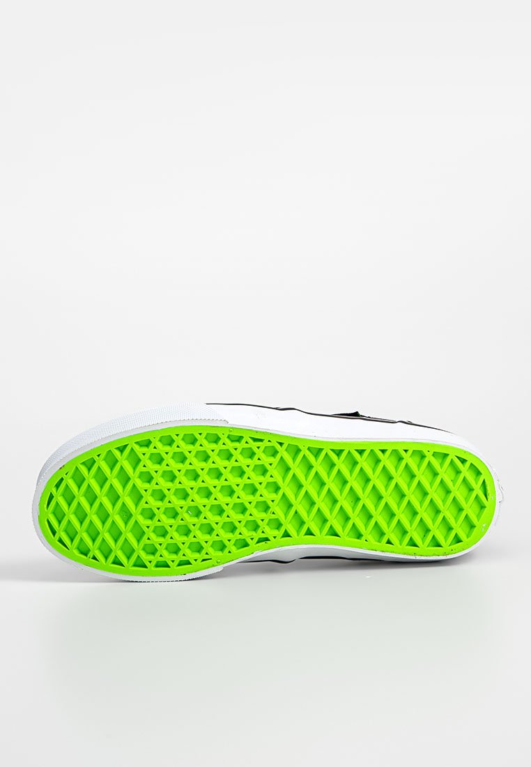 Schwarze Sneaker-Sohle mit einem lebhaften grünen Gummiprofil in Diamantmuster, das sich von einem weißen Außenrand abhebt.